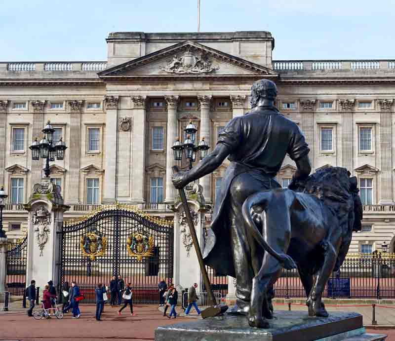 Buckingham Palace from Victoria Monument The facade behind sculpture of blacksmith with lion representing 'Manufacture'.