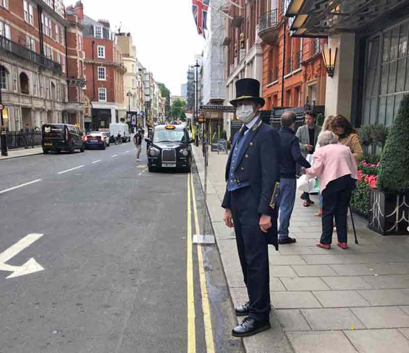 Claridge's doorman In top hat and tails with mask during lockdown.