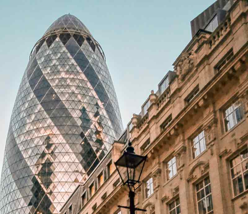 The Gherkin skyscraper Towering above a London street with classical buildings.
