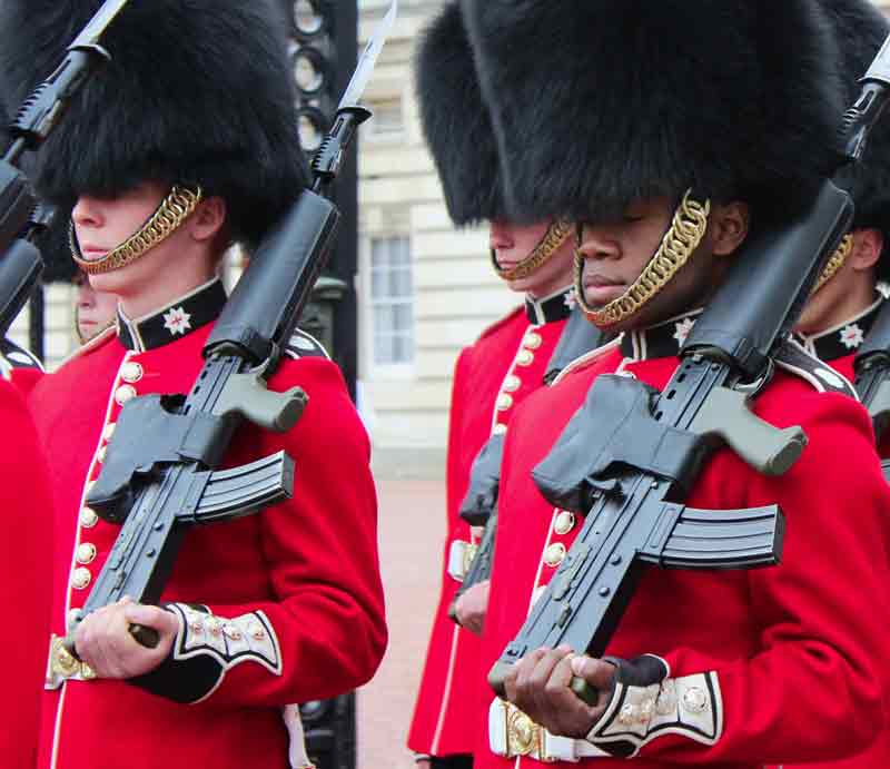 Guards Parading in red uniform with black busby hats infront of the palace.