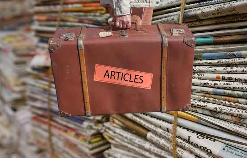 Articles Vintage brown leather suitcase with category articles label on stacked newspapers background.