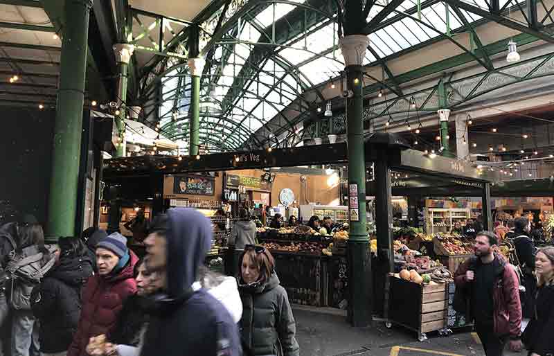Shoppers, fruit stall under Victorian wrought iron roof.