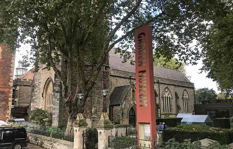 Garden Museum Victorian church and tower through trees with tall sign.