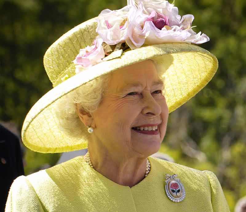 Queen Elizabeth II Smiling wearing lemon-coloured outfit with floral hat.